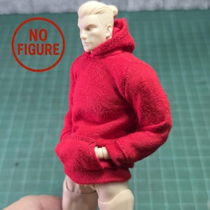 Könnte beinhalten: Ein roter Kapuzenpullover mit einer Kängurutasche. Der Sweatshirt besteht aus einem strukturierten Strickstoff. Das Bild enthält auch eine Puppenfigur, die den Sweatshirt trägt.