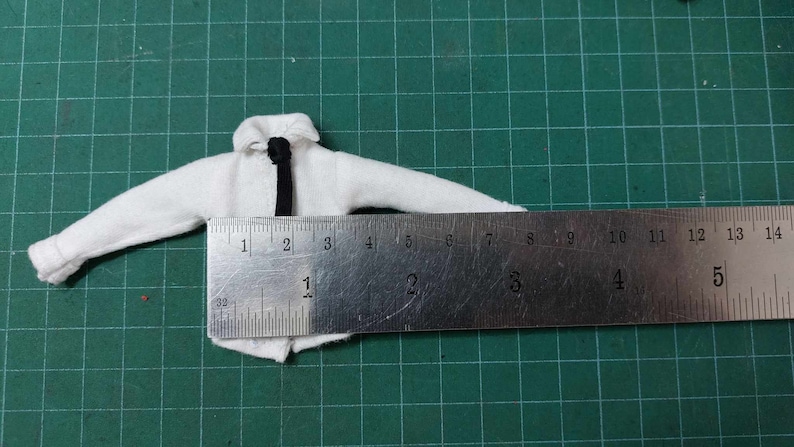 Op de afbeelding: Een wit overhemd met een zwarte stropdas, gemeten met een liniaal. De liniaal toont metingen in inches.