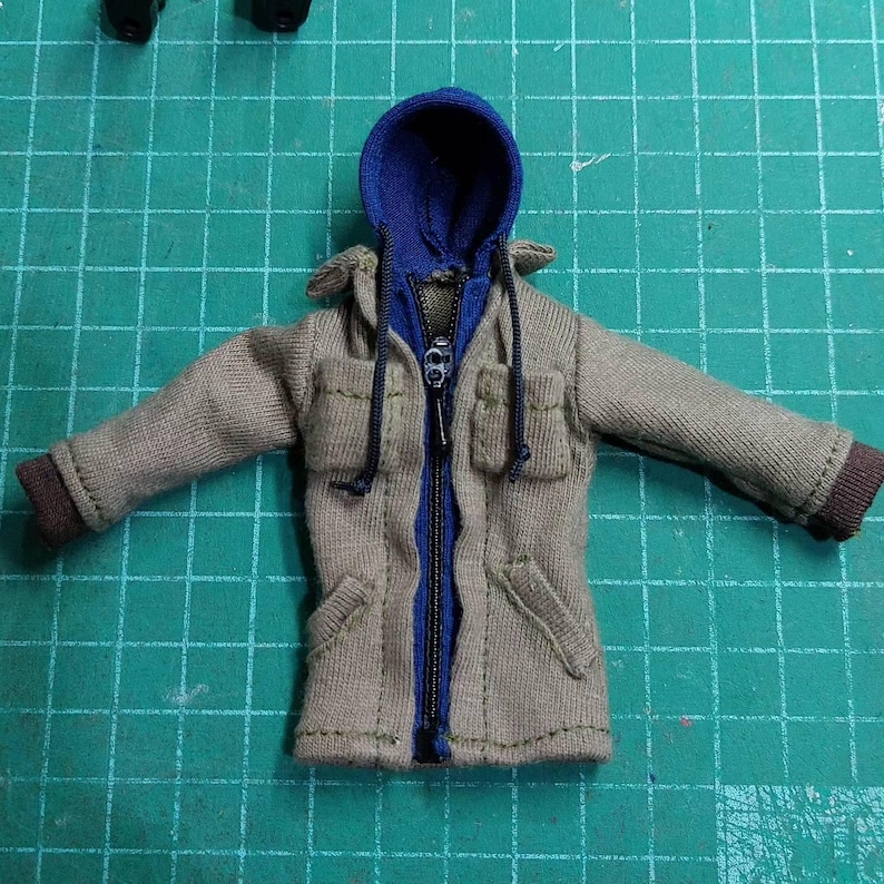 May include: A tan hooded jacket with a blue zipper and blue hood. The jacket has two pockets on the front and a drawstring hood.