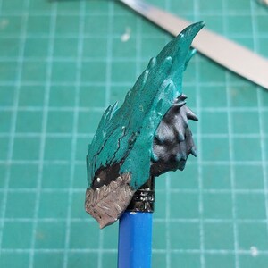 Pu&ograve; includere: Una figura di plastica color verde acqua e nero di una creatura con una testa spinosa e frastagliata. La figura &egrave; montata su una matita blu.