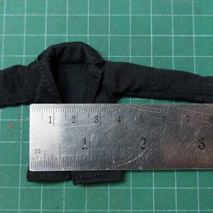 Op de afbeelding: Zwart langarm shirt met een kraag, plat gelegd op een groene ondergrond met een liniaal die 17,8 cm lang is.