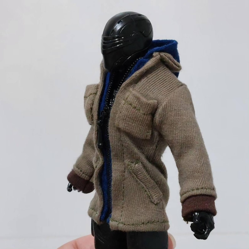 May include: A brown hooded jacket with a zip fastening and two pockets. The jacket has a blue lining and brown cuffs. The jacket is being worn by a figure with a black helmet.
