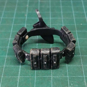 May include: A black plastic belt with multiple pouches, some of which have silver buckles. The belt is designed for action figures or dolls.