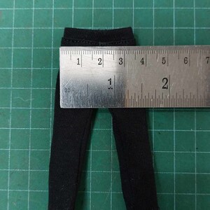 Op de afbeelding: Zwarte broek met een geribbelde textuur, gemeten met een liniaal. De broek is ongeveer 1 inch breed en 2 inch lang.