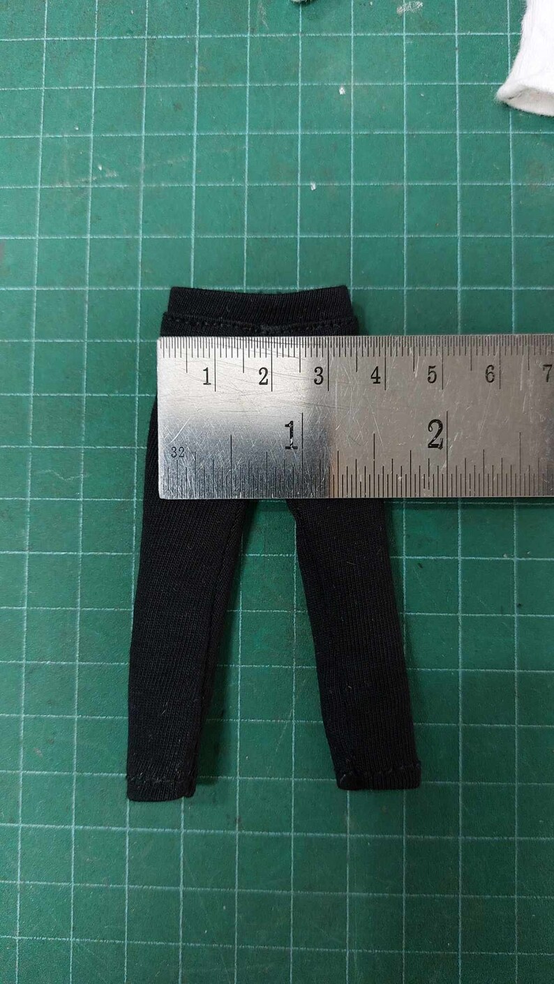 Op de afbeelding: Zwarte broek met een geribbelde textuur, gemeten met een liniaal. De broek is ongeveer 1 inch breed en 2 inch lang.