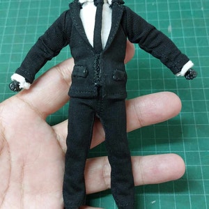 Op de afbeelding: Een zwart pak met een wit overhemd en een zwarte stropdas. Het pak is gemaakt voor een pop of een action figure.