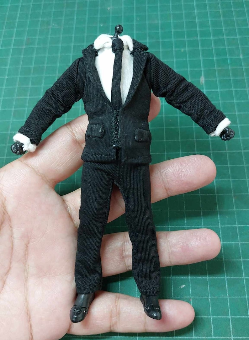 Op de afbeelding: Een zwart pak met een wit overhemd en een zwarte stropdas. Het pak is gemaakt voor een pop of een action figure.