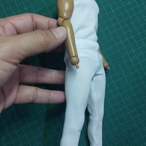 K&ouml;nnte beinhalten: Ein wei&szlig;es &auml;rmelloses Hemd und eine wei&szlig;e Hose an einer Gelenkfigur mit brauner Haut. Die Figur ist mit einem am Ellbogen gebeugten Arm posiert.