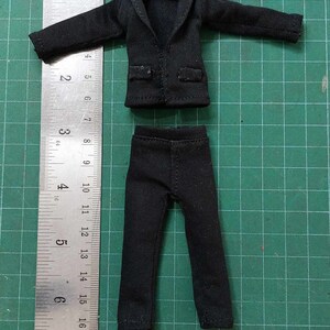 Op de afbeelding: Een zwart pak met een jas en broek. De jas heeft een kraag en lange mouwen. De broek heeft een rechte pijp.