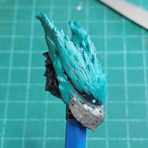 Pu&ograve; includere: Una figura in miniatura dipinta in turchese e argento di una creatura con una testa spinosa e piumata. La figura &egrave; montata su un bastone blu.