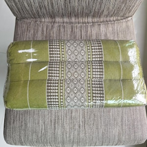 May include: A rectangular green pillow with a geometric pattern in white and brown, wrapped in clear plastic. The pillow is on a gray chair with a striped pattern.