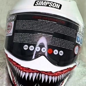 Può includere: Casco da moto Simpson bianco con visiera nera e un design minaccioso a sorriso dentato in rosso e bianco. Il casco presenta il logo Simpson e indicatori di taglia. Un design unico e accattivante per i motociclisti.