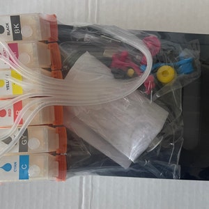 Puede incluir: Un juego de seis cartuchos de tinta para una impresora, empaquetados en plástico transparente con una impresora negra a la derecha. Los cartuchos están etiquetados con los colores cian, magenta, amarillo, negro y rojo. Los cartuchos están conectados a la impresora con tubos transparentes.