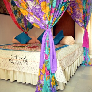 May include: A bed with a white sheet and a colorful floral patterned canopy. The canopy is made of multiple layers of fabric in shades of purple, pink, blue, and yellow. The text "Colors & Weaves" is visible on the bedspread.