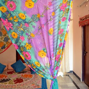 May include: A colorful floral patterned canopy bed curtain with a teal blue trim. The curtain is tied back with a knot and hangs over a bed with a patterned bedspread. The bedspread features a repeating pattern of elephants.