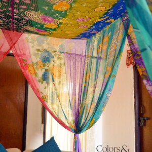 May include: A colorful canopy made of fabric with floral patterns hangs over a couch with two blue pillows. The fabric is draped in a way that creates a sense of privacy and intimacy. The text "Colors & Weaves India" is visible in the bottom right corner of the image.