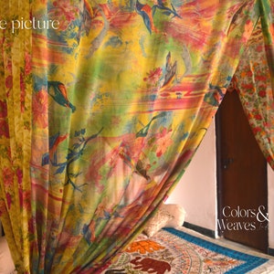 May include: A colorful canopy bed with a floral and bird print. The canopy is made of sheer fabric and hangs from the ceiling. The bed is made up with a white sheet and a patterned rug.