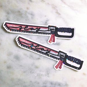 May include: Two pink and white glitter stickers of a chainsaw with the word "sexy" written on it.