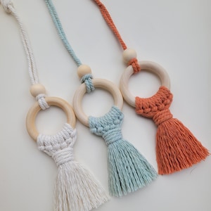 May include: Three wooden ring toys with tassels. The rings are natural wood with white, light blue, and orange tassels.