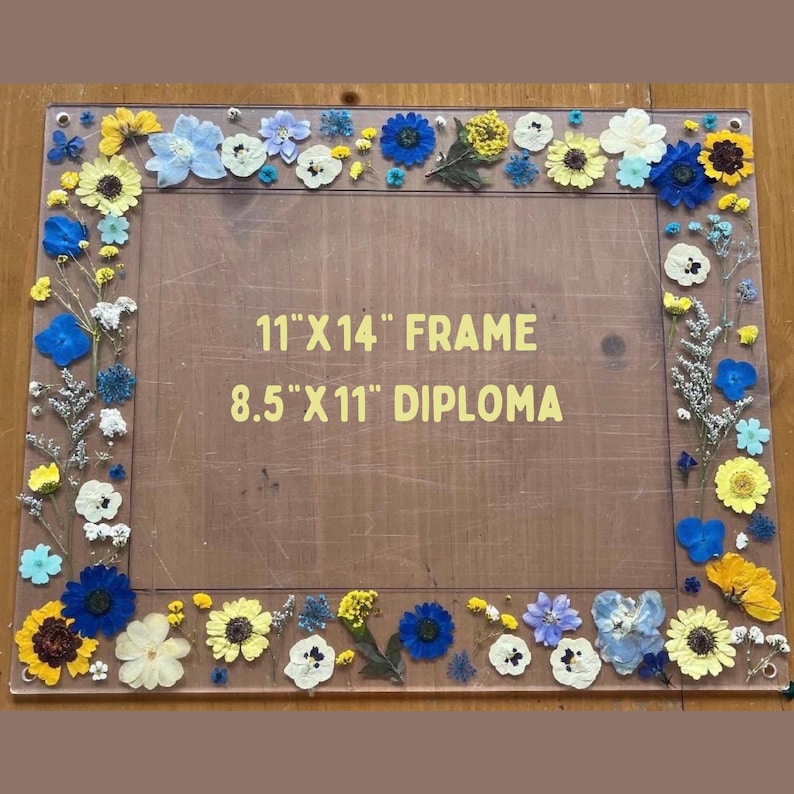 Pode incluir: Uma moldura retangular com fundo de madeira, adornada com uma variedade de flores secas coloridas. A moldura foi projetada para conter uma foto ou obra de arte de 28 cm x 36 cm, com espa&ccedil;o para um diploma de 22 cm x 28 cm. As flores incluem flores amarelas, azuis e brancas.