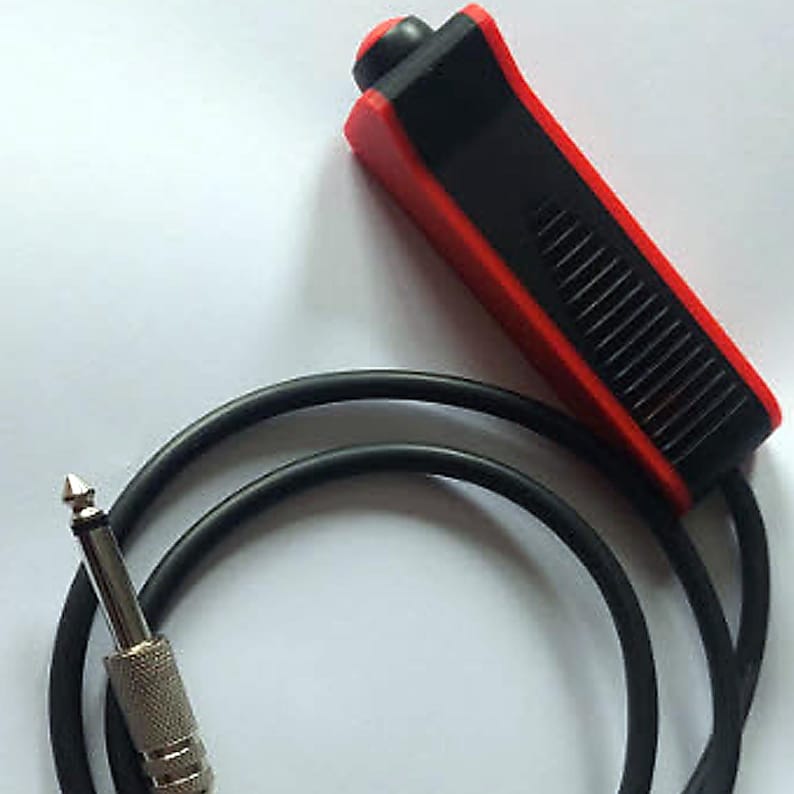 May include: A black and red guitar foot switch with a black cable and a silver-colored plug. The foot switch has a red top and sides with a black center section. The cable is coiled and the plug has a pointed tip.