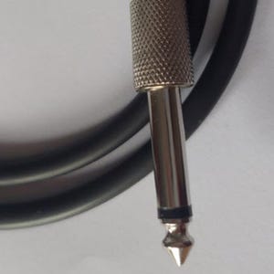 May include: Close-up of a silver-colored audio cable connector with a textured grip and a pointed tip. A black cable is visible in the background, curving away from the connector. The connector is designed for audio equipment.