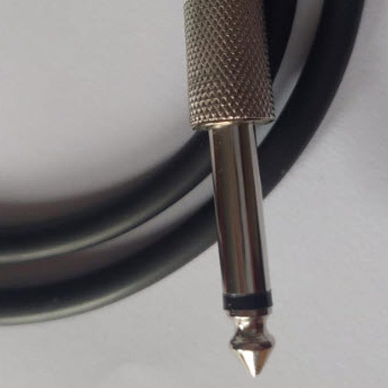 May include: Close-up of a silver-colored audio cable connector with a textured grip and a pointed tip. A black cable is visible in the background, curving away from the connector. The connector is designed for audio equipment.
