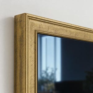 Può includere: Uno specchio da parete rettangolare caratterizzato da una spessa cornice decorata con finitura oro anticato. La cornice presenta un profilo a gradini multistrato con una sottile patina scura, che circonda una superficie in vetro liscia.