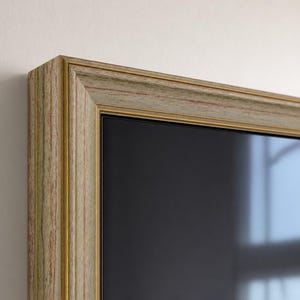 May include: A rectangular picture frame featuring a multi-layered design with a light green and tan wood-grain finish, accented by thin gold-toned inner and outer trim lines, surrounding a dark, reflective, and smooth glass surface.