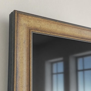 Può includere: Uno specchio da parete rettangolare caratterizzato da un'ampia cornice decorata con una finitura anticata color oro e marrone scuro. La cornice presenta un profilo a gradini con profonde scanalature lungo il bordo esterno, attorno a una superficie riflettente.