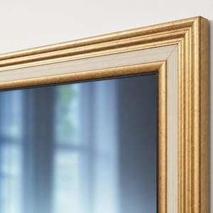 Op de afbeelding: Een rechthoekige fotolijst met een gelaagd ontwerp, voorzien van een getextureerde gouden buitenrand en een gladde, licht crèmekleurige binnenrand. De lijst omsluit een donker, reflecterend oppervlak met een wazig, licht interieur.