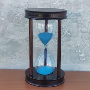 Peut inclure: Un sablier en bois avec un sablier bleu. Le sablier est sur une surface en bois.