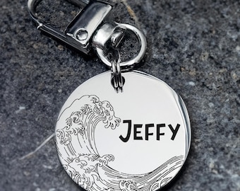 May include: A silver-colored, round pet tag with the name "JEFFY" in a bold font. The tag features a detailed wave design. It includes a metal clasp for easy attachment to a pet's collar.
