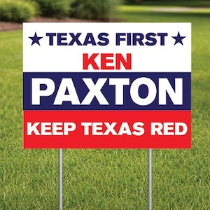 May include: A rectangular political yard sign with a white background at the top featuring the text TEXAS FIRST in dark blue with stars on each side. Below is the name KEN PAXTON in red and white text on a blue stripe, and KEEP TEXAS RED in white.