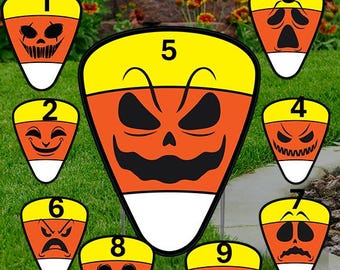 May include: A set of nine Halloween-themed yard stakes shaped like candy corn. Each stake features a different jack-o'-lantern face in orange, black, yellow, and white. The stakes are designed for outdoor decoration.