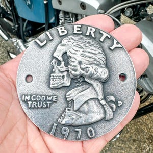 Op de afbeelding: Een zilverkleurige metalen munt met een schedel en gekruiste beenderen ontwerp. De munt heeft de woorden "LIBERTY", "IN GOD WE TRUST" en "1970" erop gegraveerd.