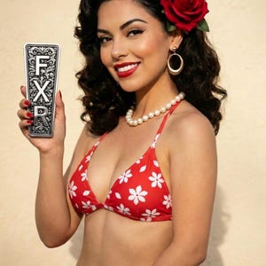 Puede incluir: Una mujer con un bikini rojo con estampados florales blancos, un collar de perlas y pendientes de aro dorados. Tiene una rosa roja en el pelo y sostiene un objeto rectangular plateado con las letras "FXR".