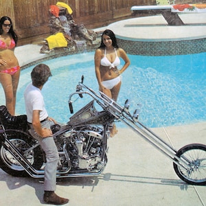 Puede incluir: Una motocicleta cromada con una horquilla delantera larga y un asiento individual. La motocicleta est&aacute; aparcada junto a una piscina con dos personas en traje de ba&ntilde;o de pie en el agua.