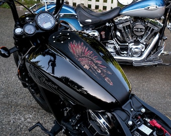May include: A black Indian motorcycle with a detailed headdress design on the fuel tank. The motorcycle has a glossy finish, chrome accents, and a speedometer. Another motorcycle is visible in the background.
