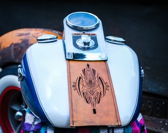 May include: Close-up of a motorcycle gas tank. The tank is white with a blue stripe and a brown leather panel with a black design. The tank has a chrome speedometer and the text "THE SIXTYNINERS.COM".