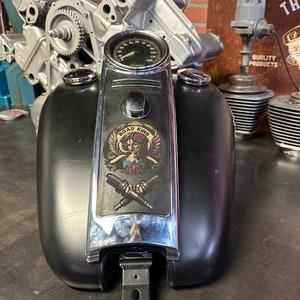 Könnte beinhalten: Schwarzer Motorrad-Benzintank mit Chromleiste und einem Aufkleber mit der Aufschrift "Road King" mit einer Frau in einer geflügelten Krone, die eine Rose hält.