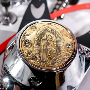 Op de afbeelding: Een verchroomd motoronderdeel met een rond, verguld deksel met een reliëfbeeld van de Maagd Maria. Het deksel heeft een gedetailleerd ontwerp met bloemmotieven.