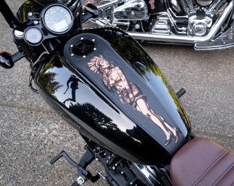 May include: Black motorcycle fuel tank with a leather panel featuring a Native American woman illustration. The tank has a glossy finish, with gauges and handlebars visible. The seat is brown.