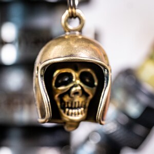 Puede incluir: Un llavero de calavera dorado con un dise&ntilde;o de casco. La calavera tiene una cara detallada con una sonrisa de dientes.