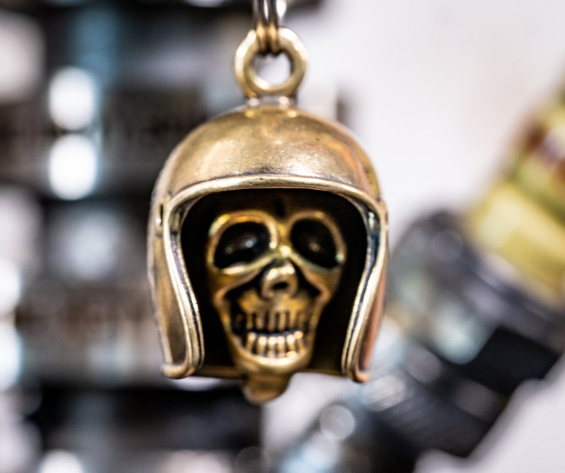 Puede incluir: Un llavero de calavera dorado con un dise&ntilde;o de casco. La calavera tiene una cara detallada con una sonrisa de dientes.
