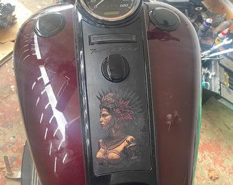 May include: A burgundy motorcycle gas tank with a black panel featuring a Native American woman illustration and the text "Road King". The tank has two black round caps and a white stripe design.