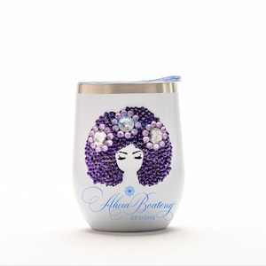 May include: A white stainless steel tumbler featuring a graphic of a silhouette with a large afro hairstyle embellished with purple and lavender rhinestones. The text Alicia Boateng DESIGNS is printed in blue script below the graphic.