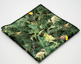 May include: A square pocket square with a jungle-themed pattern. The design features lush green foliage, toucans, lemurs, and other colorful birds and animals. The pocket square has a black border.