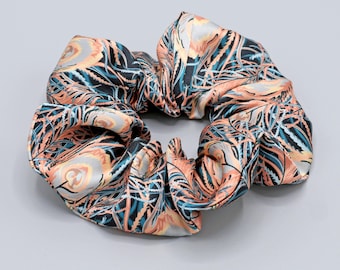 May include: A peach, teal, and black patterned scrunchie made of satin.
