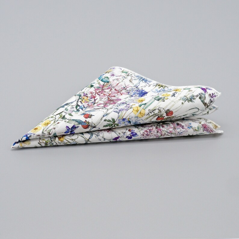 May include: A white cotton pocket square with a floral print featuring a variety of colorful flowers and leaves.